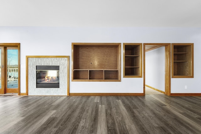 unfurnished living room with a multi sided fireplace, built in shelves, baseboards, and wood finished floors