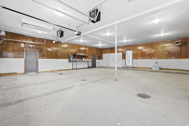 garage featuring electric panel, a garage door opener, and wood walls