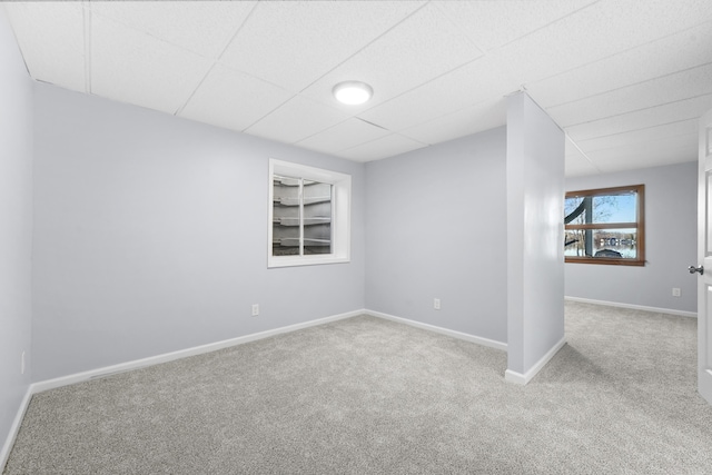 carpeted spare room with built in features, a drop ceiling, and baseboards