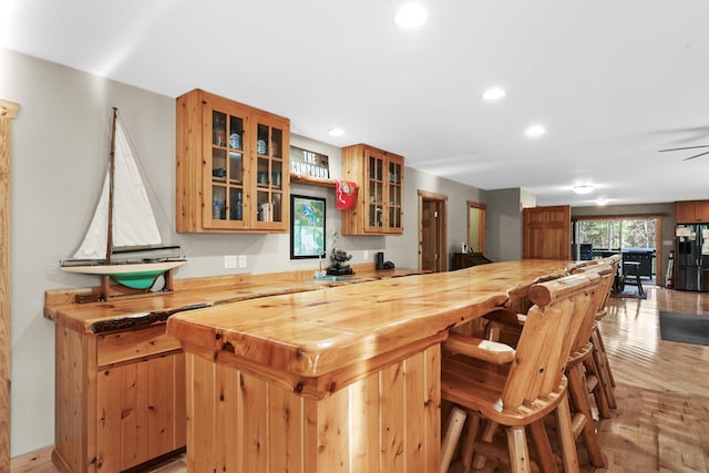 bar featuring bar, recessed lighting, black fridge with ice dispenser, and light wood-style floors