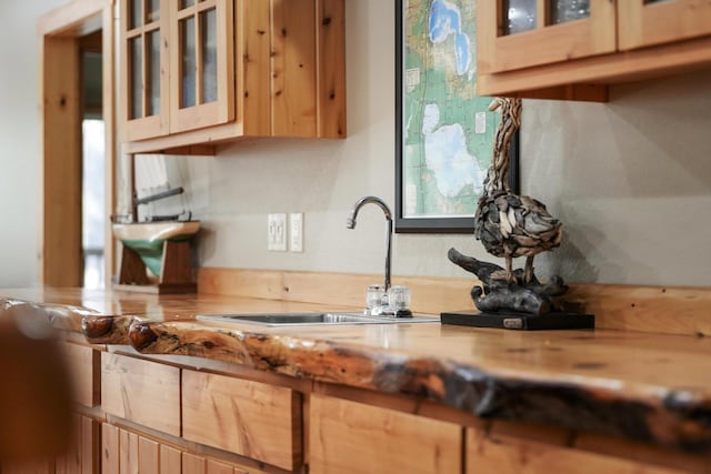 kitchen featuring light brown cabinets, light countertops, glass insert cabinets, and a sink