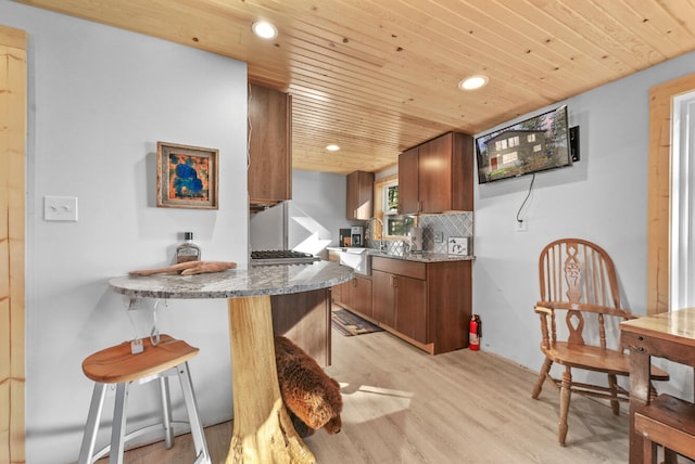 kitchen featuring wooden ceiling, light wood finished floors, brown cabinetry, and backsplash