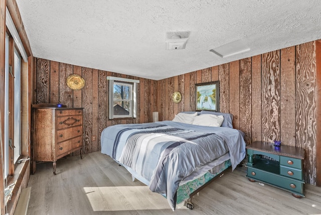 bedroom with attic access, wooden walls, wood finished floors, and a textured ceiling