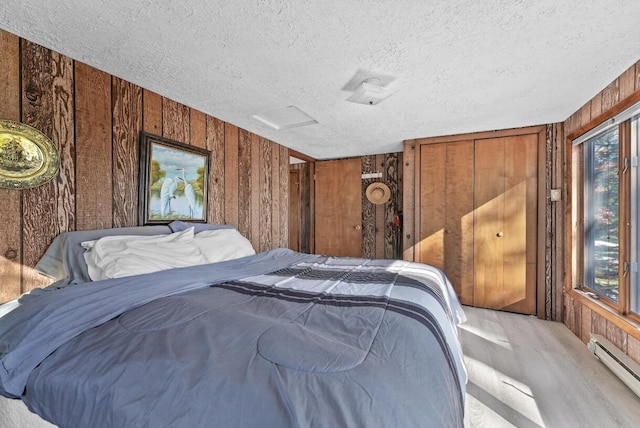 bedroom featuring wood walls, a textured ceiling, attic access, and a baseboard radiator