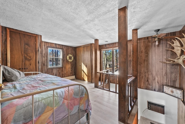 bedroom with baseboard heating, wood finished floors, wood walls, and a textured ceiling