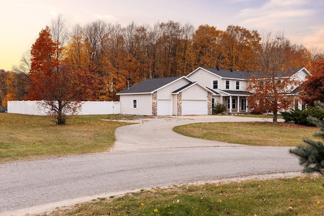 view of front facade with stone siding, driveway, a front yard, and fence