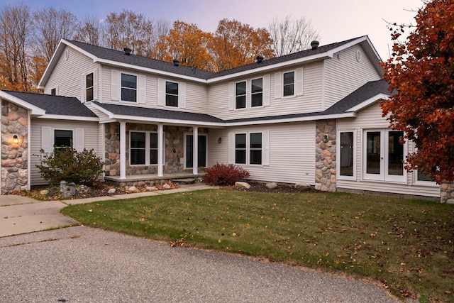 traditional-style house with a front lawn, stone siding, and roof with shingles