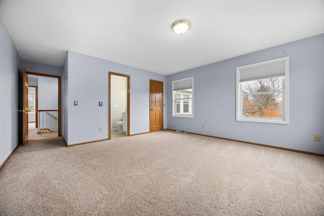 unfurnished bedroom with multiple windows, ensuite bath, baseboards, and carpet floors