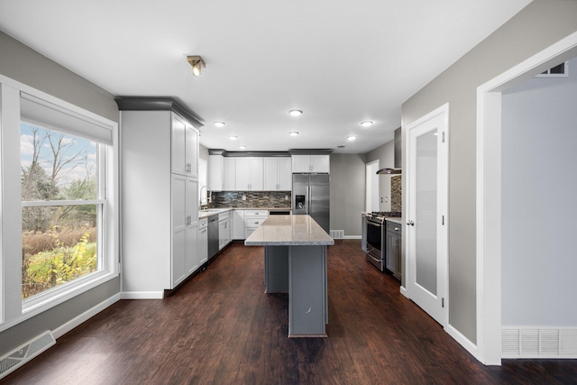 kitchen featuring light stone countertops, visible vents, stainless steel appliances, decorative backsplash, and dark wood-type flooring