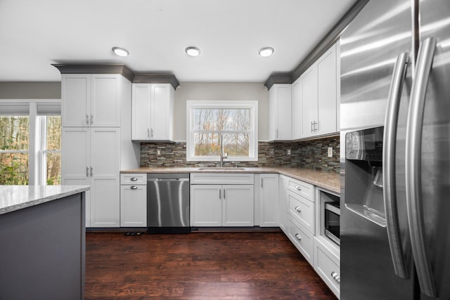 kitchen featuring light stone countertops, dark wood finished floors, a sink, stainless steel appliances, and backsplash