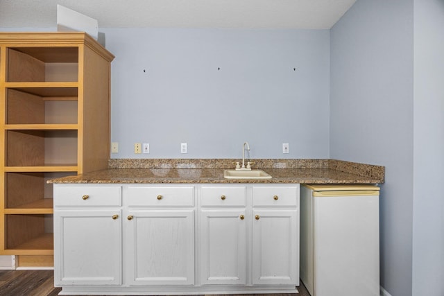 kitchen with dark stone countertops, white cabinets, wood finished floors, and a sink