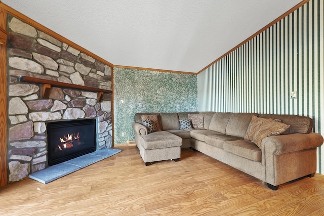 living area with ornamental molding, a textured ceiling, wood finished floors, a stone fireplace, and lofted ceiling