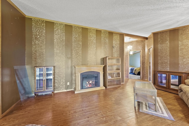 living area featuring a glass covered fireplace, baseboards, a textured ceiling, and wood finished floors