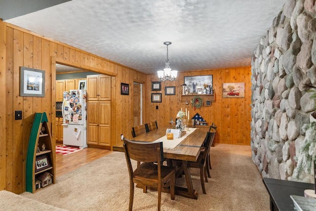 dining area featuring ornamental molding, a textured ceiling, wooden walls, an inviting chandelier, and light colored carpet