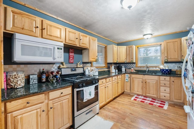 kitchen featuring white microwave, stainless steel range with gas cooktop, light wood-style flooring, light brown cabinetry, and a sink