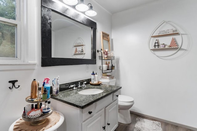 bathroom featuring toilet, ornamental molding, wood finished floors, baseboards, and vanity