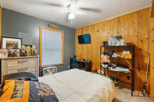 carpeted bedroom featuring wooden walls and a ceiling fan