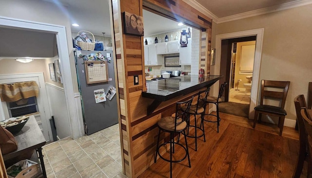 kitchen featuring dark countertops, light wood finished floors, freestanding refrigerator, white cabinets, and crown molding