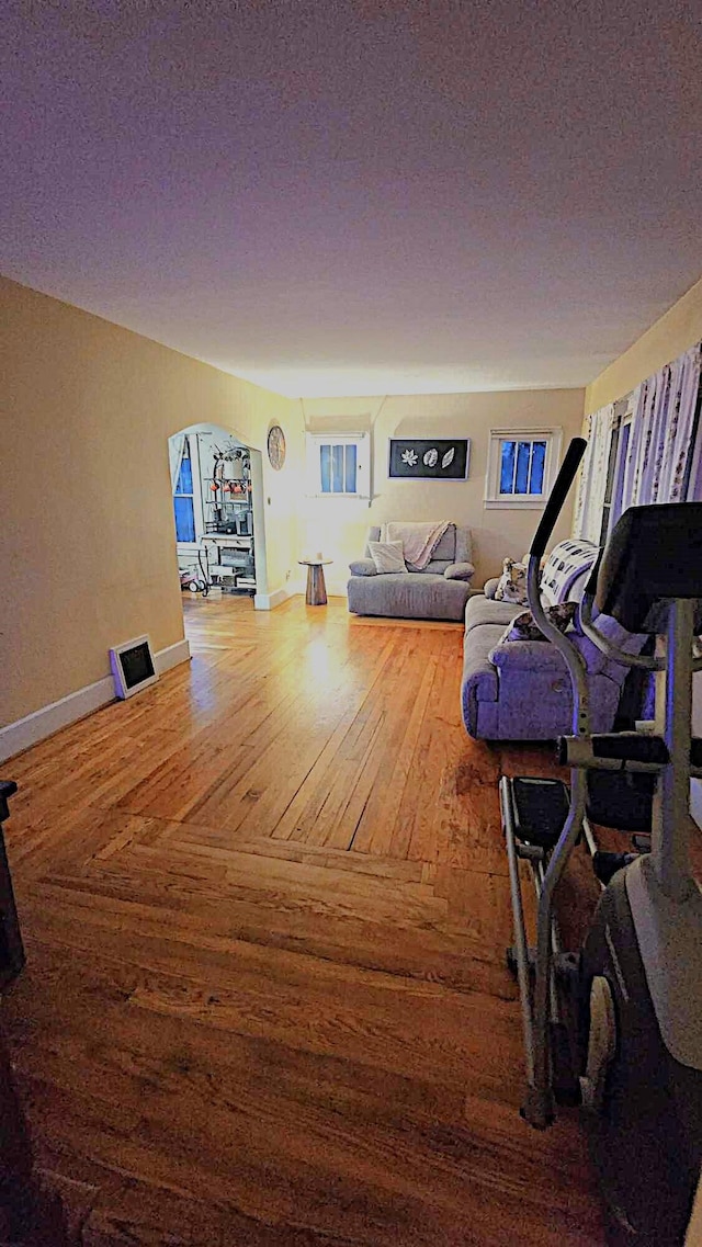 living area featuring arched walkways, a textured ceiling, baseboards, and wood finished floors