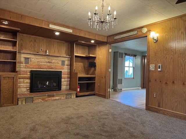 unfurnished living room featuring built in features, carpet floors, an inviting chandelier, a fireplace, and wood walls