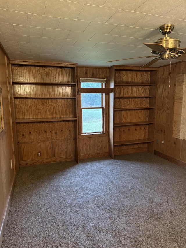 carpeted spare room with built in features, wood walls, and ceiling fan