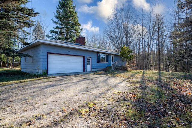 exterior space with an attached garage, a chimney, and dirt driveway