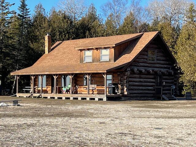 view of front of property with log siding, covered porch, and a chimney