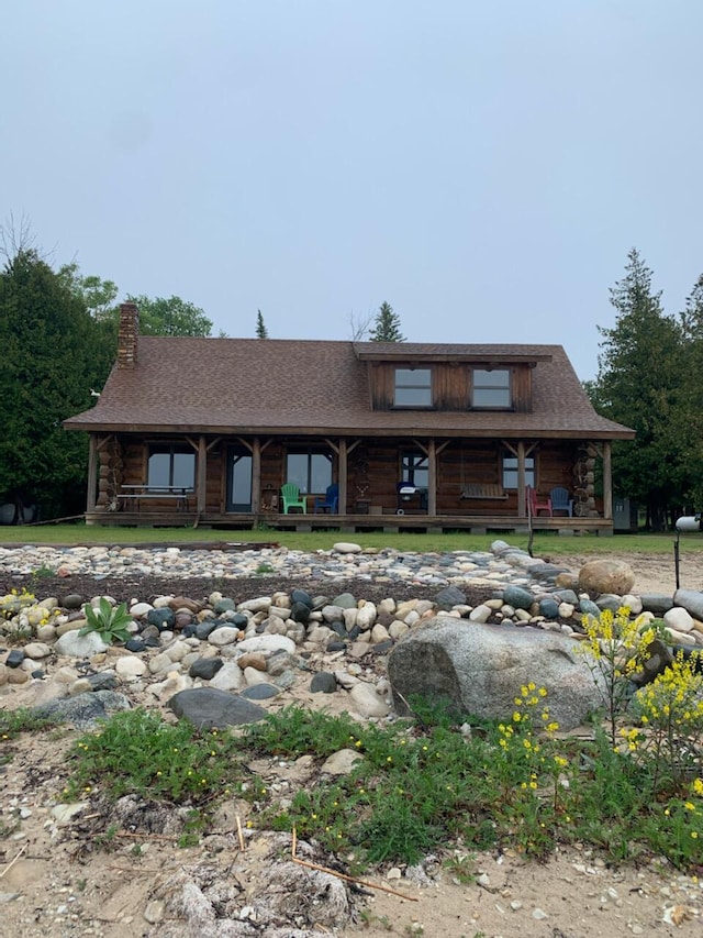 log cabin featuring covered porch, log exterior, and a chimney