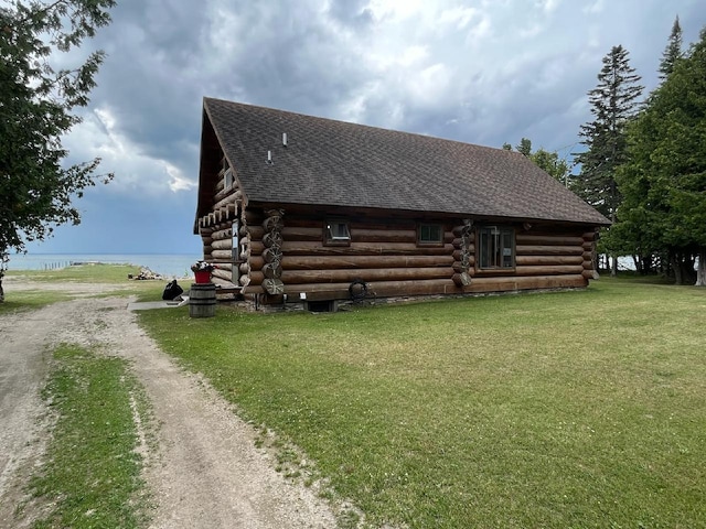 view of side of property with driveway, a shingled roof, a water view, log exterior, and a lawn