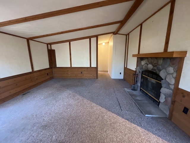 unfurnished living room with heating unit, carpet, lofted ceiling with beams, a stone fireplace, and wood walls