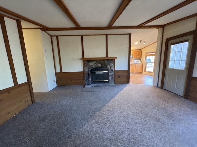 unfurnished living room with a stone fireplace, wood walls, lofted ceiling with beams, and carpet