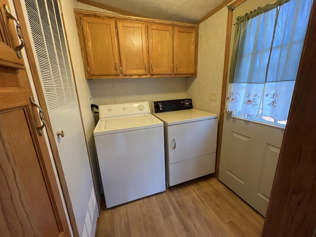 laundry area featuring washing machine and clothes dryer, cabinet space, a textured ceiling, and light wood-style flooring