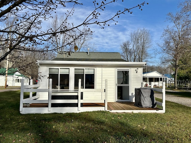 rear view of house featuring a wooden deck, a yard, and roof with shingles