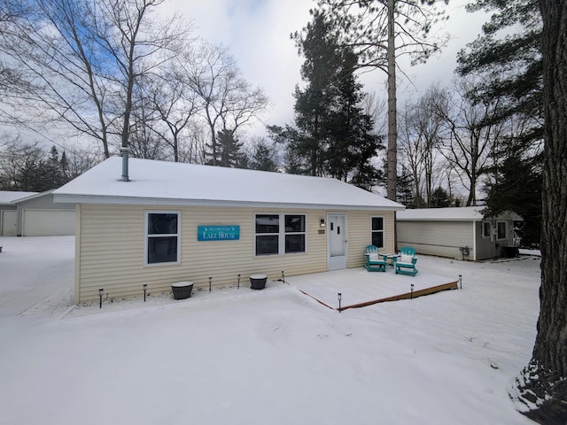 snow covered house featuring an outbuilding, a wooden deck, and a detached garage