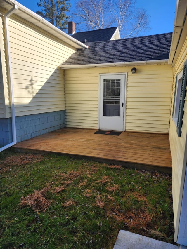 view of exterior entry with a wooden deck, a chimney, and a shingled roof