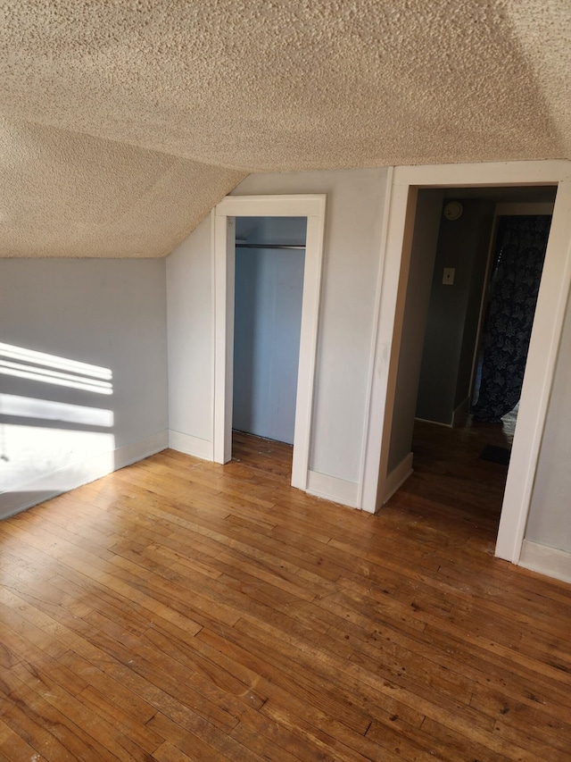 unfurnished bedroom featuring hardwood / wood-style flooring, a textured ceiling, a closet, baseboards, and lofted ceiling