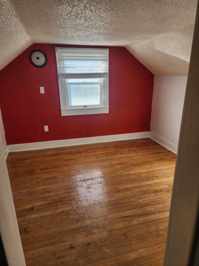 additional living space featuring baseboards, a textured ceiling, and hardwood / wood-style flooring