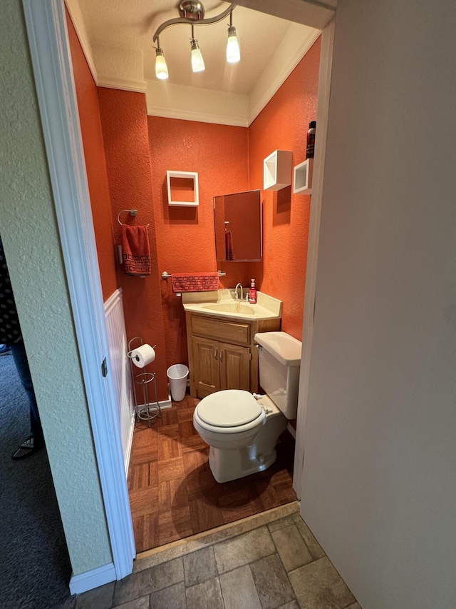 half bathroom with toilet, crown molding, vanity, and a textured wall