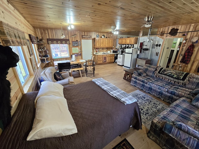 bedroom featuring light wood-style floors, wood ceiling, wooden walls, and freestanding refrigerator