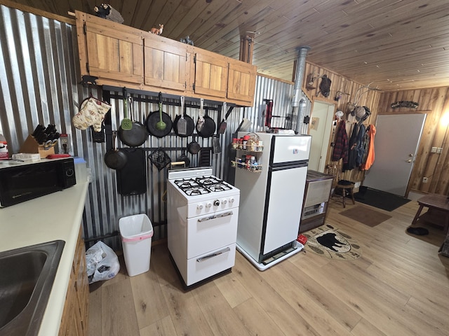 kitchen featuring wood walls, light wood-style flooring, wooden ceiling, white appliances, and a sink