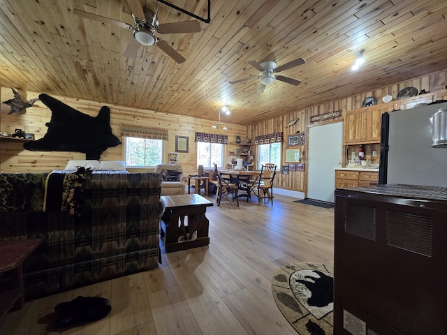 living room featuring a ceiling fan, wooden walls, light wood-style flooring, and wooden ceiling