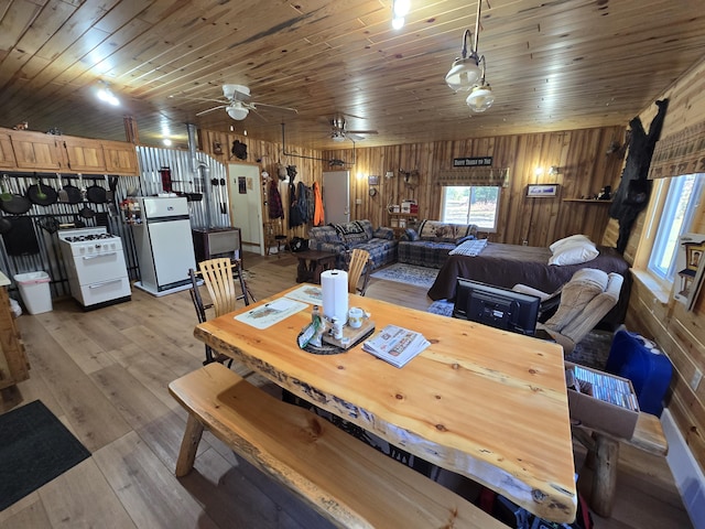 dining room with ceiling fan, light wood-type flooring, wooden walls, and wooden ceiling