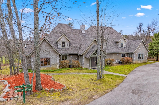 view of front of home with a front lawn, a chimney, stone siding, and stucco siding