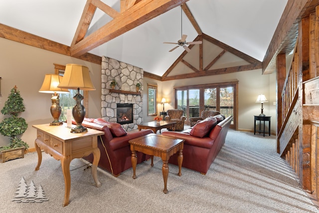 living area featuring beamed ceiling, light colored carpet, stairs, a stone fireplace, and a ceiling fan