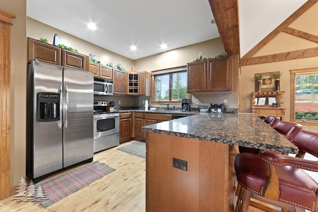 kitchen featuring light wood-type flooring, a sink, a kitchen breakfast bar, stainless steel appliances, and a peninsula