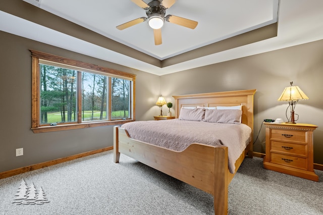 carpeted bedroom with a tray ceiling, baseboards, and a ceiling fan