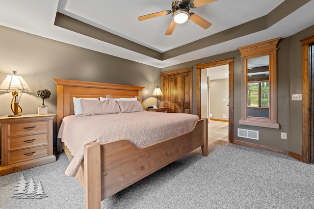 bedroom featuring light carpet, visible vents, baseboards, and a tray ceiling