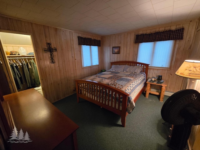 carpeted bedroom with a spacious closet, baseboard heating, wood walls, and a closet