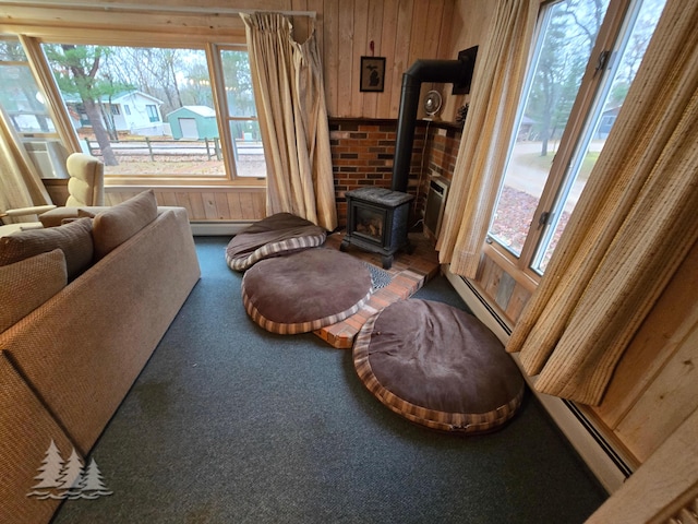 living room featuring wooden walls, baseboard heating, a wood stove, and carpet floors