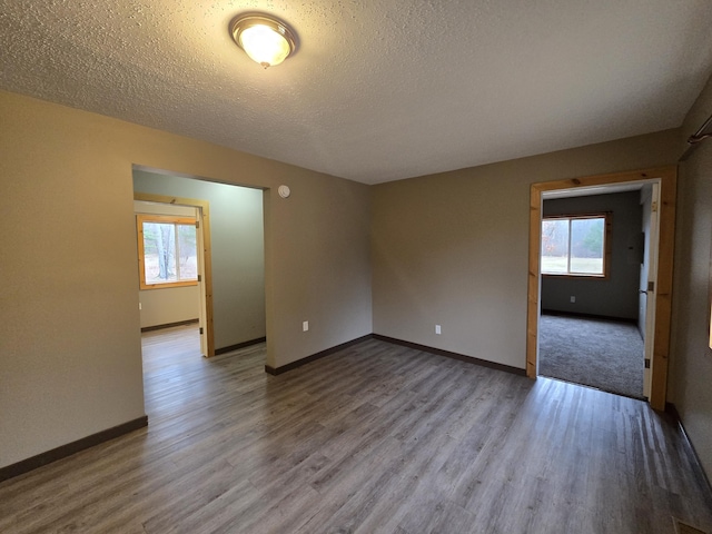 unfurnished room with a textured ceiling, baseboards, and wood finished floors